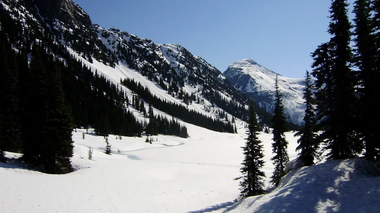 Frozen Long Lake in the Phelix Creek cirque, snow covered slopes and dark conifers rising to a pyramidal peak under a clear sky