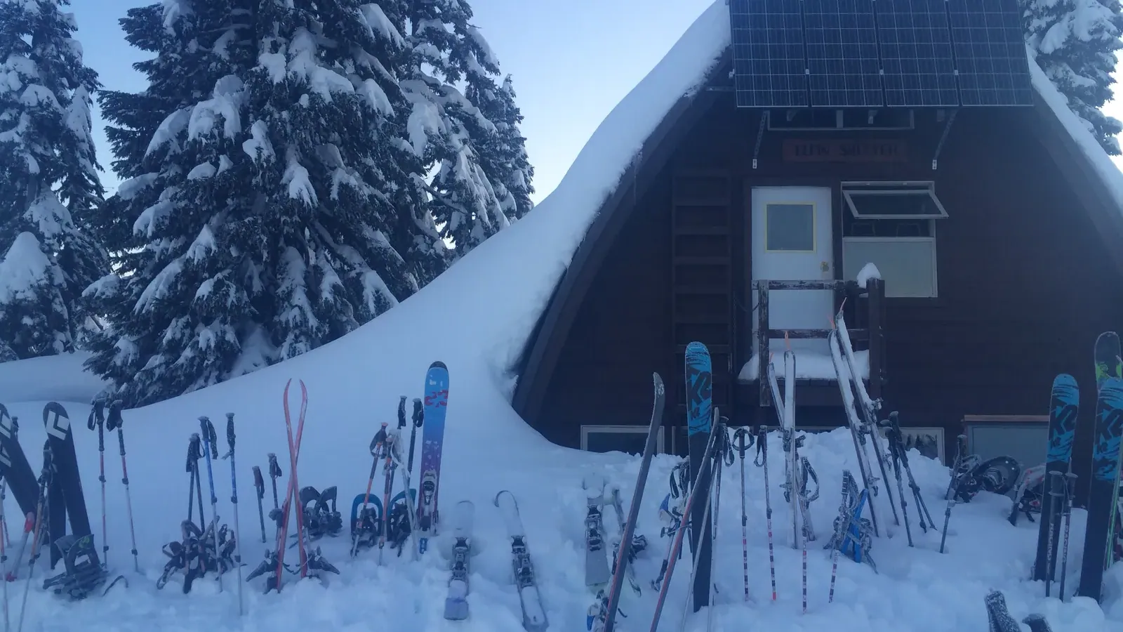 The Elfin Lakes shelter buried in snow, with skis and snowshoes stacked outside the entrance.