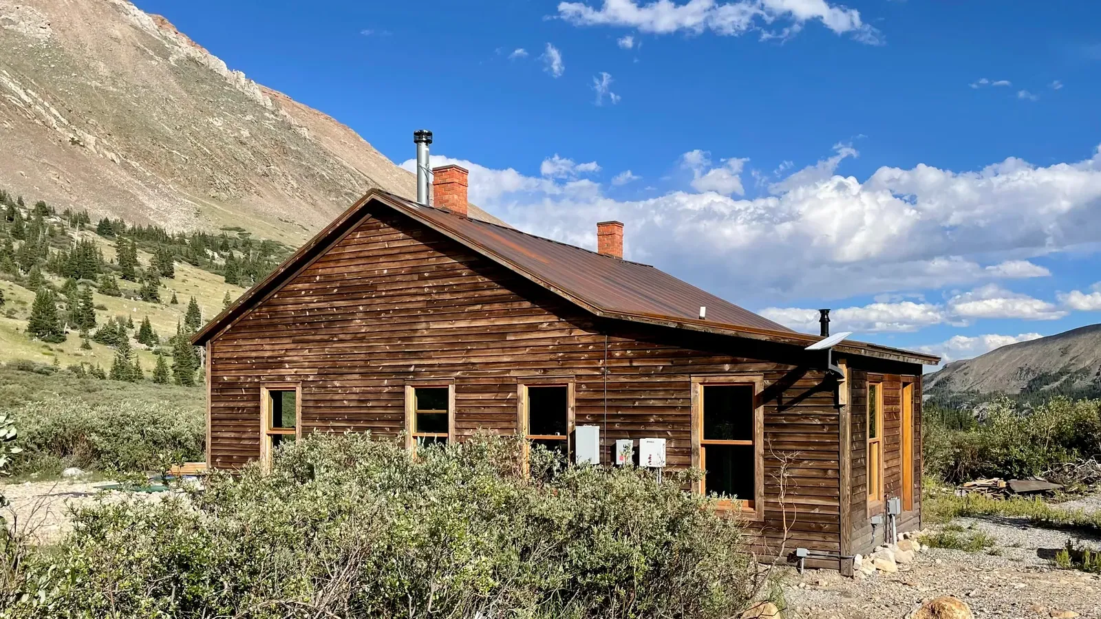 The restored 1883 North London Mill office, a wood-sided cabin with a metal roof and brick chimneys, below the Mosquito Range near Alma, Colorado