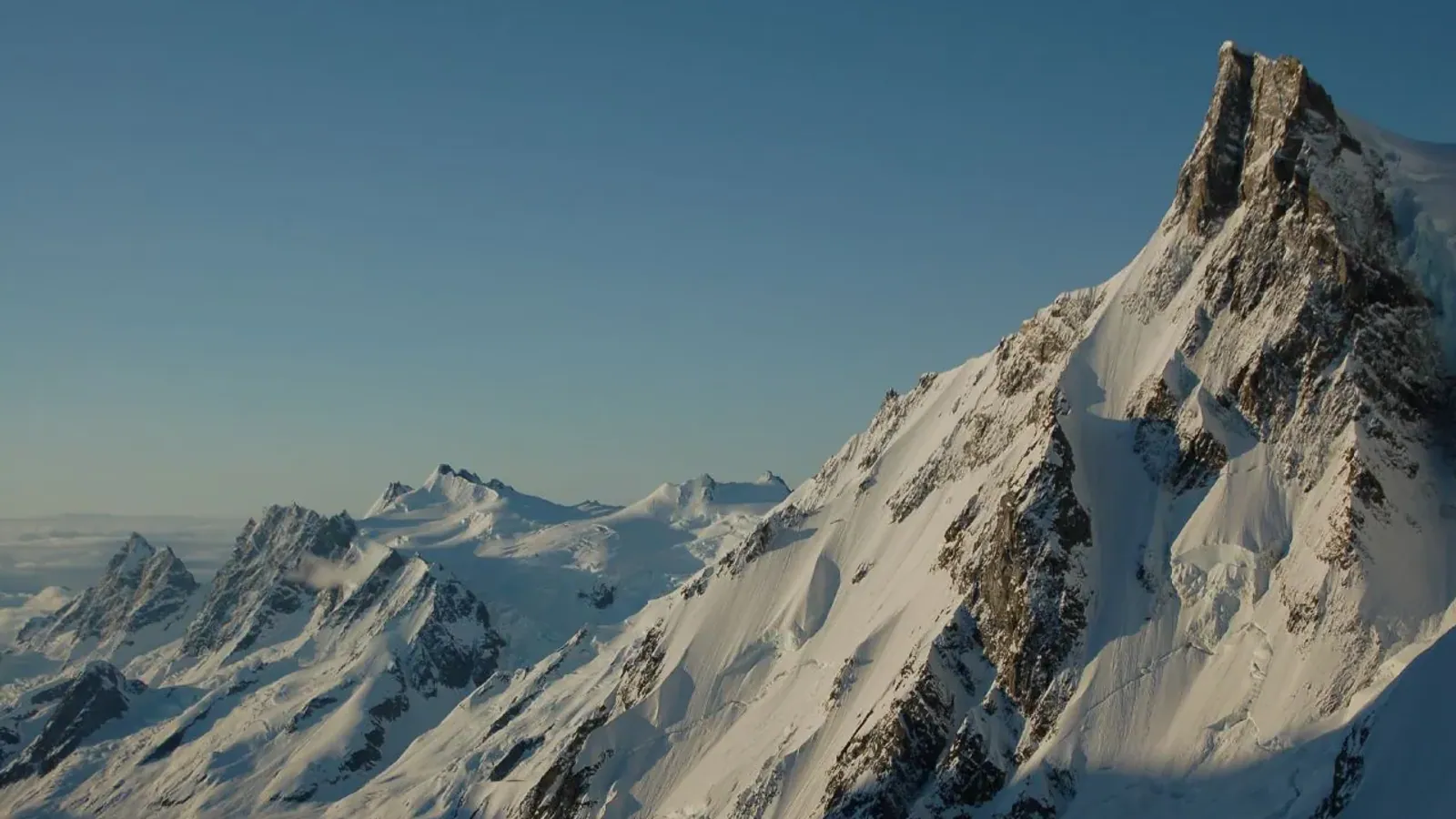 Evening light on the snow covered northwest face of Bravo Peak in the Waddington Range, with a line of glaciated summits running away to the left under a deep blue sky